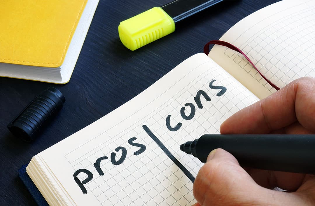 hand with pen writing pros and cons list of outsourcing marketing